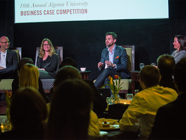 man sitting in group on stage addressing the audience