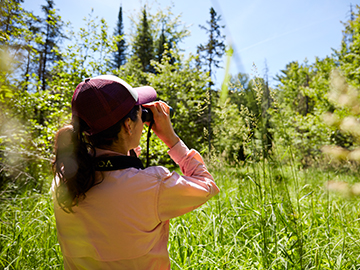student looking into binoculars in the forest
