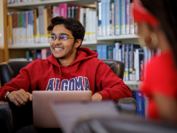 Student smiling in library wearing Algoma u sweater